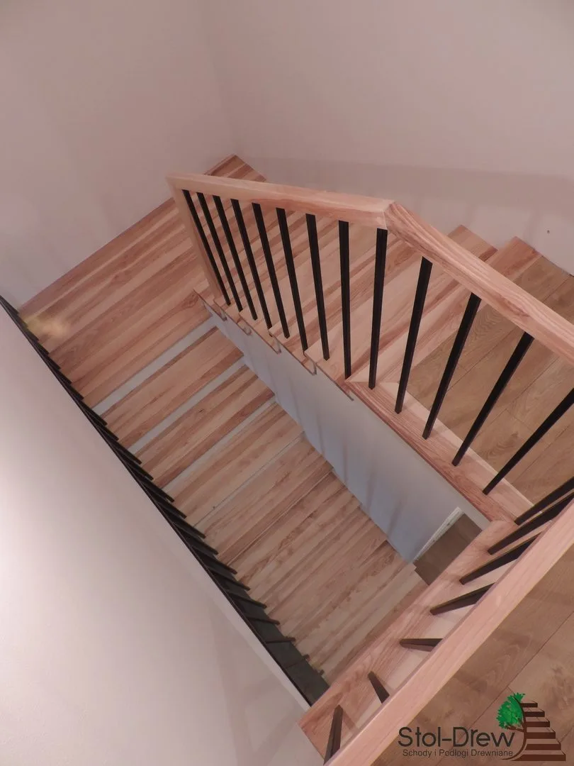 Widok z piętra na pochwyt z jesionu i czarne pręty balustrady nad dwoma biegami — Dukla