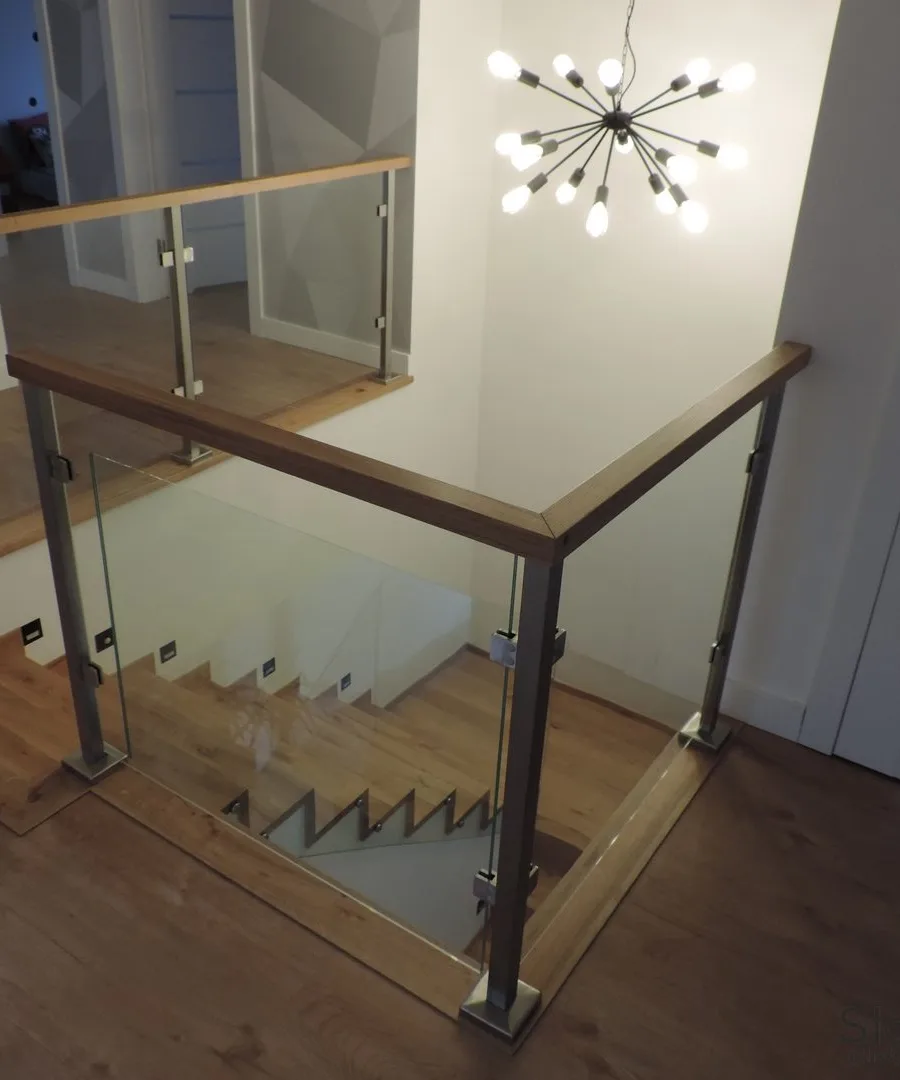 Narożnik szklanej balustrady z drewnianym pochwytem przy otworze, w tle żyrandol — Przeworsk