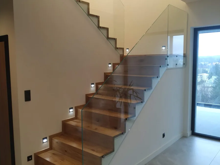 Schody dywanowe ze szklaną balustradą i światłami w ścianie
