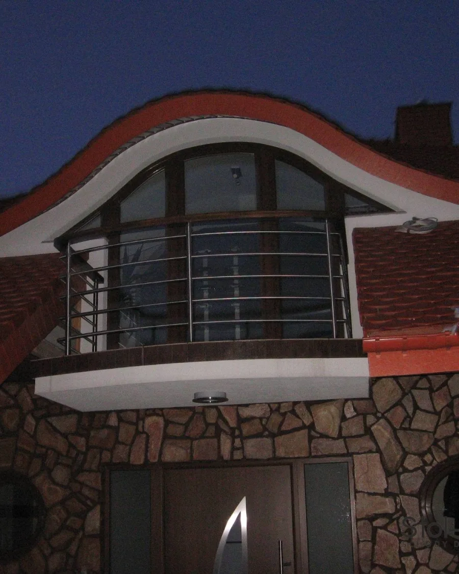Łukowa balustrada zewnętrzna z poziomych rurek nierdzewnych na balkonie pod dachem, widok wieczorem